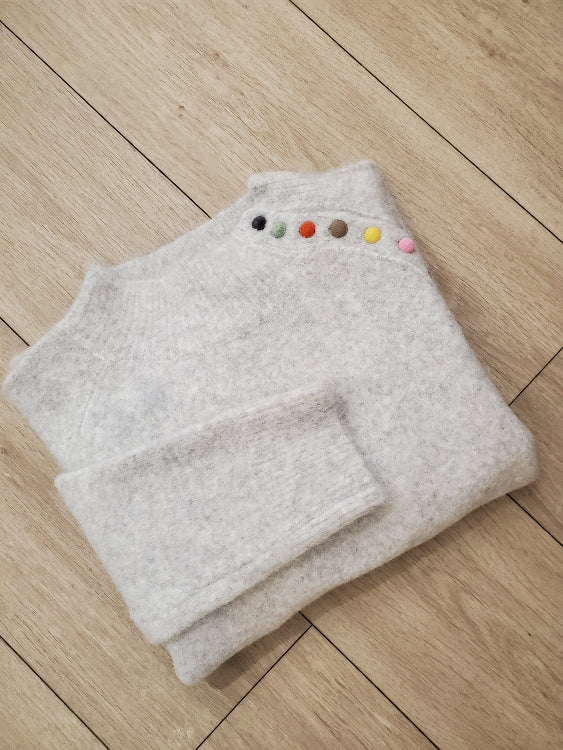 Pull gris chiné col montant avec boutons multicolore. Photo plié.