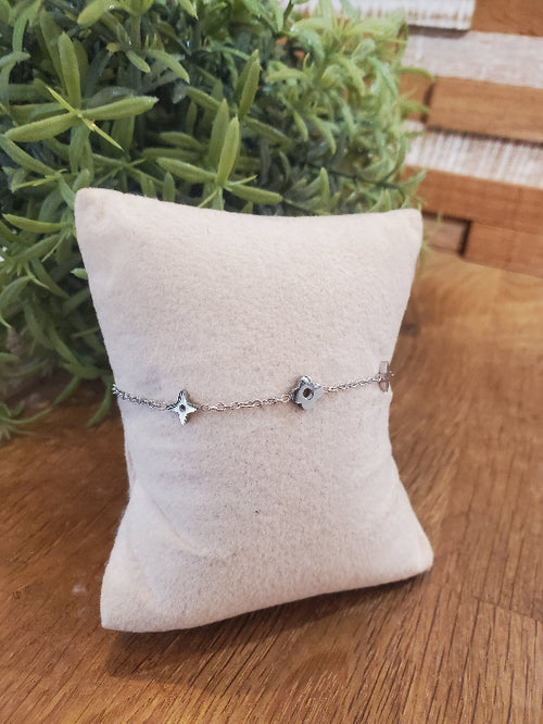 Bracelet en chaine fine avec étoile et trèfle incrusté. colorie Argent photo sur un coussin de présentation.
