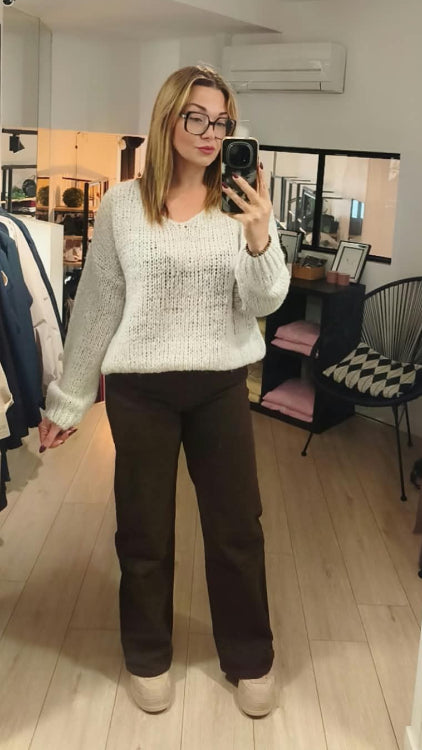 Pull V colorie beige porté avec un jean droit marron. 