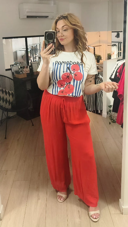 T-shirt imprimé d'une grappe de tomate sur un fond de rayures bleu foncé. Photo porté avec un pantalon fluide corail. 