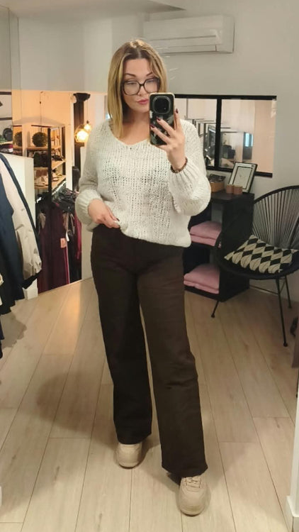 Pull V colorie beige porté avec un jean droit marron. 