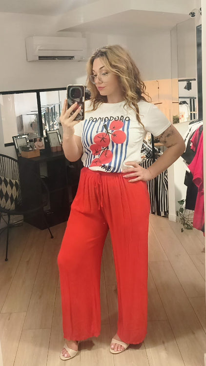 T-shirt imprimé d'une grappe de tomate sur un fond de rayures bleu foncé. Photo porté avec un pantalon fluide corail. 