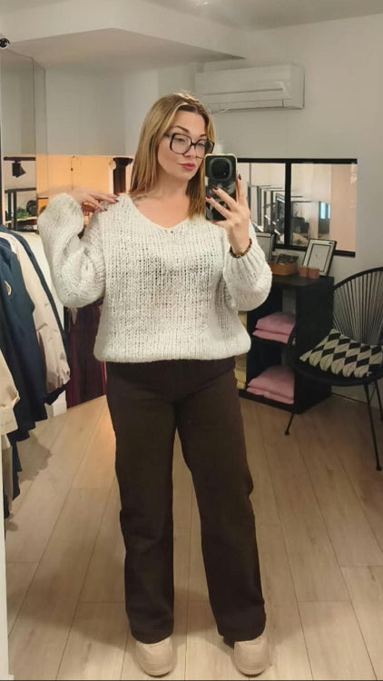 Pull V colorie beige porté avec un jean droit marron. 