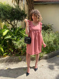 Robe sans manches avec volant rose porté avec un petit sac noir et une paire d'escarpins vernis.