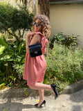 Robe sans manches avec volant rose porté avec un petit sac noir et une paire d'escarpins vernis.