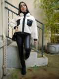 Veste bi matière blanche et noir porté avec un jean enduit noir, un sac en fausse fourrure et des bottines fourrées